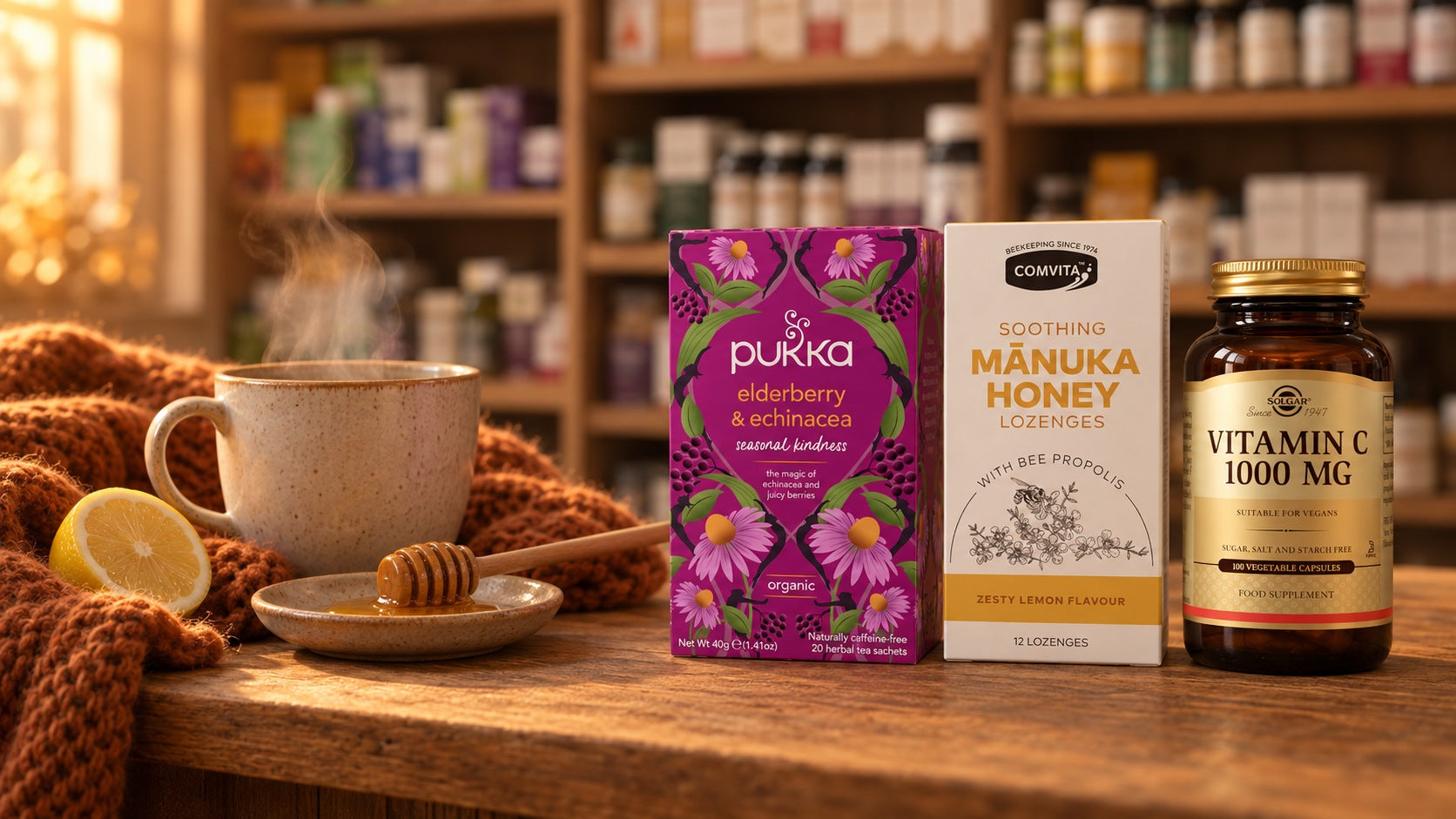 Pukka Elderberry and Echinacea tea, Comvita Manuka Honey Lozenges and Solgar Vitamin C 1000 mg on a wooden shop counter beside a mug of tea, honey dipper, lemon and knitted scarf